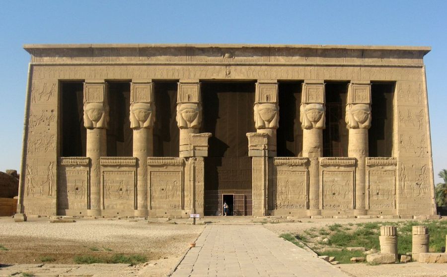 The facade of the temple of Hathor at Dendera: six massive columns carved with the face of Hathor, the wall between them covered in relief and hieroglyphic text.